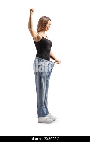 Junge Frau, die Gewichtsverlust feiert und eine alte Jeans auf weißem Hintergrund anprobiert Stockfoto