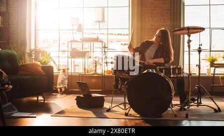 Junge Frauen spielen Schlagzeug während einer Bandprobe in einem Loft Studio bei warmem Sonnenlicht am Tag. Talentiertes Schlagzeugermädchen, das vor einem Live-Konzert auf der Bühne mit anderen Musikern praktiziert. Stockfoto