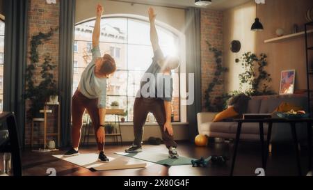 Positives Seniorenpaar, das Gymnastik und Yoga Dehnübungen zusammen zu Hause am sonnigen Morgen macht. Konzept des gesunden Lebensstils, Fitness, Freizeit, Paarziele, Wohlbefinden und Ruhestand. Stockfoto