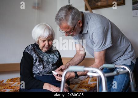 Der Mann hilft einer älteren Frau bei alltäglichen Aufgaben, hilft bei der Technologie und stellt mit ihrer Familie Videoaufnahmen über das Smartphone ein Stockfoto