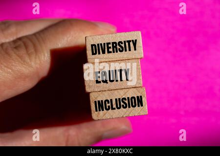 Wörter für Vielfalt, Gerechtigkeit und Einbeziehung auf Holzblock mit rosafarbenem Hintergrund. Konzeptionelle Vielfalt, Gerechtigkeit und Inklusion DEI Symbol. Kopierbereich. Stockfoto