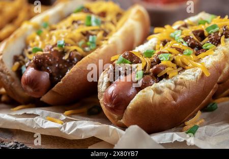 Großaufnahme von zwei Chili Hot Dogs mit gehacktem Cheddar und gehackten grünen Zwiebeln auf Pergamentpapier Stockfoto