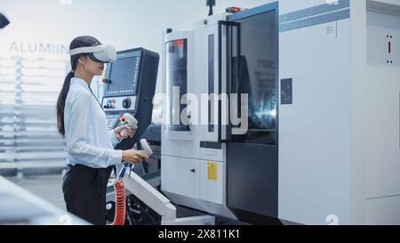 Ingenieurin mit Virtual Reality-Headset und Betrieb einer schweren Industriemaschine mit Controllern in einer Fabrik. Techniker, der Industriemaschinen mit Hilfe der VR-Technologie konfiguriert. Stockfoto