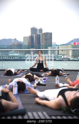 Yogalehrerin und ihre Schüler machen Meditation im Freien an der Wan Chai Promenade in Hongkong, China Stockfoto