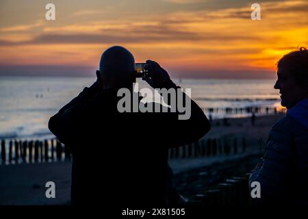 Sonnenuntergang am Strand von Zoutelande, Strand mit Holzpfahlbrüchen, Touristen, Zeeland, Niederlande Stockfoto