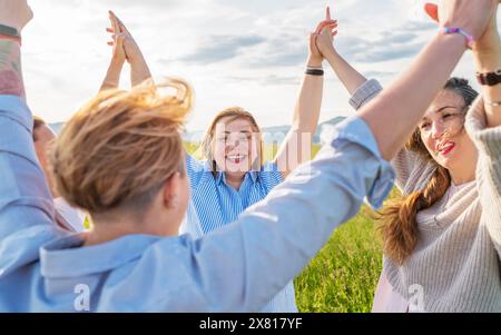 Porträt von vier fröhlich lächelnden und lachenden Frauen, die Hand in Hand halten und während des Sonnenuntergangs im Freien am grünen Hügel entlang gehen. Freundin der Frau Stockfoto