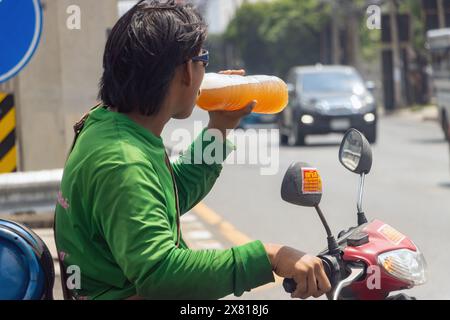 SAMUT PRAKAN, THAILAND, 12. MAI 2024, Ein Motorradfahrer trinkt Ein Getränk aus einer Plastikflasche, während er an einer Kreuzung wartet Stockfoto