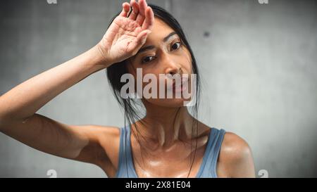 Starke asiatische Frau wischt Schweiß von der Stirn ab, schaut in die Kamera. Das Konzept des erfolgreichen Engagements von Frauen gegen Ungerechtigkeiten und Vorurteile. Stilvolles Porträt Im Kinoformat Stockfoto