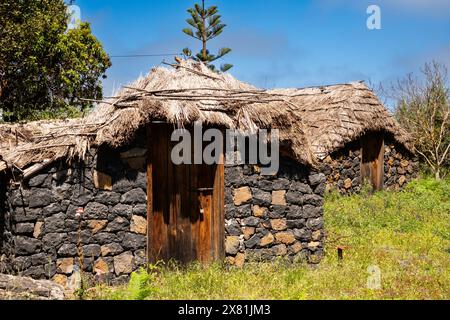 Eine kleine Hütte mit einem Strohdach steht auf einem Hügel. Die Hütte ist aus Stein und hat eine Holztür. Die Hütte ist von Gras und Bäumen umgeben Stockfoto