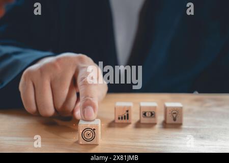 Geschäftsmann wählt mit dem Finger Holzblöcke mit der Geschäftsstrategie und dem Aktionsplan aus, die auf das Geschäftskonzept ausgerichtet sind.Geschäftsentwicklungskonzept. Emot Stockfoto