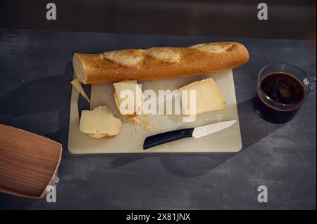 Stillleben, Frühstück von oben auf dem Küchentisch. Eine Tasse frisch gebrühten Espresso in der Nähe eines Schneidebretts mit einem Vollkorn-Baguette und einem Laib davon Stockfoto