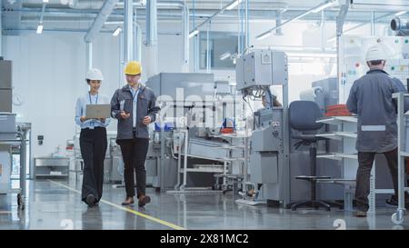 Porträt zweier junger asiatischer Schwerindustrietechniker in Hart-Hüten mit Laptop-Computer, der in einer Fabrik spricht. Aufnahmen von zwei Fertigungsmitarbeitern bei der Arbeit in der Produktionsstätte. Stockfoto