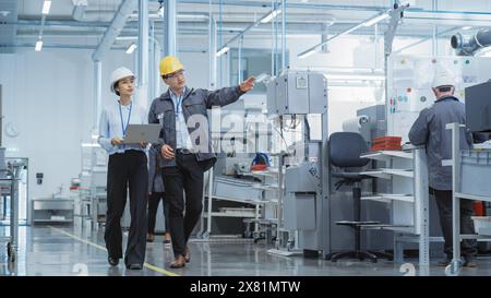 Porträt zweier junger asiatischer Schwerindustrietechniker in Hart-Hüten mit Laptop-Computer, der in einer Fabrik spricht. Aufnahmen von zwei Fertigungsmitarbeitern bei der Arbeit in der Produktionsstätte. Stockfoto