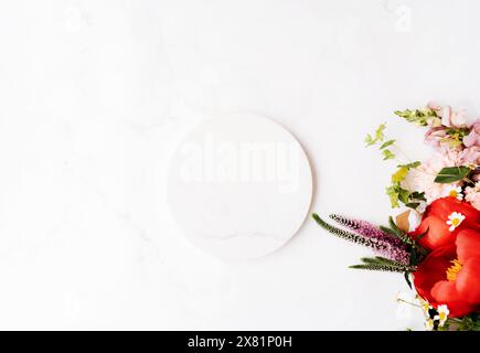 Weißes Marmorpodium mit rundem Podium und Blumenstrauß mit roter Pfingstrose und anderen Blumen auf weißem Tisch mit Kopierraum für Ihren Text von oben und flachem Lay-Stil. Platzieren Stockfoto