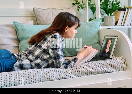 Eine Schülerin, die zu Hause mit einem Laptop liegt und Videounterricht hat Stockfoto