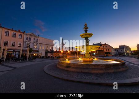 Beleuchteter Masaryk-Platz in Karviná am Abend bei Sonnenuntergang, Stadtzentrum von Karviná, Brunnen im Vordergrund, Kirche im Hintergrund, Stadtplatz Stockfoto