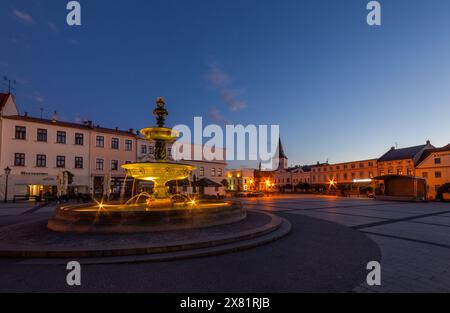 Beleuchteter Masaryk-Platz in Karviná am Abend bei Sonnenuntergang, Stadtzentrum, Brunnen im Vordergrund, Kirche im Hintergrund Stockfoto