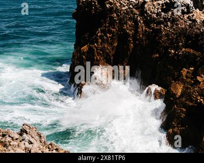 Ein atemberaubender Blick von oben auf die Wellen des Ozeans, die gegen die braunen, strukturierten Felsen krachen. Stürmisches Meer, Blick von oben. Sturmsaison, Meereslandschaft Backgro Stockfoto