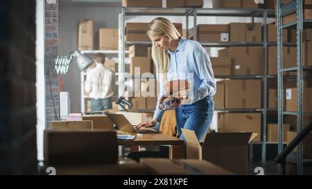 Inventory Manager verpackt einen stilvollen Fahrradsitz, der online an einen Kunden verkauft wird. Ein kleines Papppaket für das Porto vorbereiten. Blonde weibliche Eigentümerin kleiner Unternehmen, die im Lager arbeitet. Stockfoto