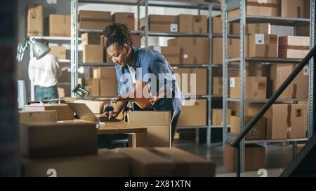 Besitzer eines kleinen Unternehmens, der einen stilvollen Fahrradsitz verpackt, der online an einen Kunden verkauft wird. Einen kleinen Karton für das Porto vorbereiten. Black Female Inventory Manager, der in der Lagereinrichtung arbeitet. Stockfoto