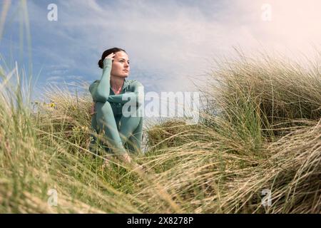 Sportliche Frau, die in Sanddünen sitzt und sich entspannt. Stockfoto