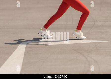 Nahaufnahme, Tiefwinkelansicht einer sportlichen Frau, die mit Pfeil auf Asphalt läuft Stockfoto