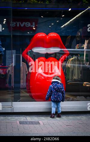 Ein kleines Kind steht vor einem Schaufenster, fasziniert von alarmierenden roten Lippenskulpturen. The Rolling Stones Shop, Carnaby Street, London, England, Stockfoto