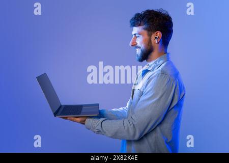 Bärtiger Mann, der Laptop im Neonlicht hält Stockfoto