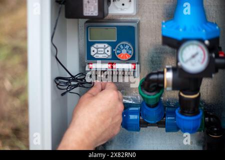 Anschluss der Stromversorgung an eine automatische Wasserversorgung für die Tropfbewässerung. Der Mann fixiert den Draht im Terminal. Stockfoto