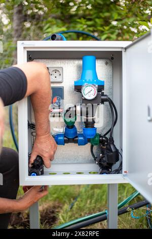 Montage eines automatischen Wasserversorgungssystems für die Tropfbewässerung. Ein Mann installiert eine Montagebox. Stockfoto