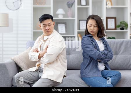 Ein Paar, das mit überkreuzten Armen getrennt auf einem Sofa sitzt und Spannungen und ungelöste Konflikte in einem modernen Wohnzimmer darstellt. Stockfoto