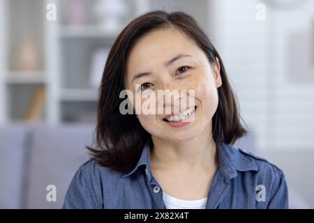 Porträt einer fröhlichen Frau in lässigem Outfit, die sich zu Hause in einem gemütlichen und hellen Wohnzimmer entspannt. Stockfoto