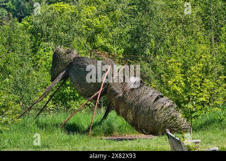 Eine große, gewebte Skulptur eines Insekts, möglicherweise einer Ameise, aus natürlichen Materialien und in einer üppigen, grünen Umgebung im Freien. Stockfoto