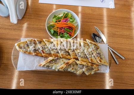 Türkische Pita mit Hackfleisch. Türkische Pizza mit Hackfleischpide und einer Schüssel Salat auf einem braunen Tisch. Stockfoto