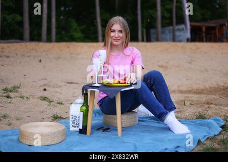 Sorglose Frauen, die draußen picknicken. Positives Modell, das auf Karo sitzt, sich umarmt, Obst und Käse isst Stockfoto