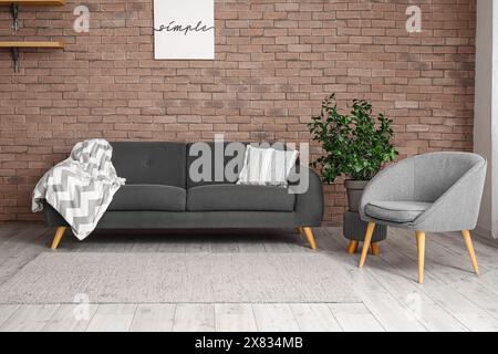 Inneneinrichtung eines modernen Wohnzimmers mit stilvollem Sessel und Sofa in der Nähe von Ziegelwänden Stockfoto