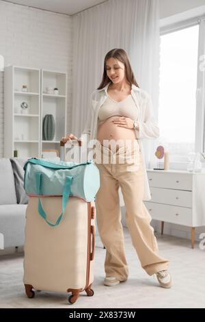 Junge schwangere Frau mit gepackter Entbindungs-Krankenhaus-Tasche und Koffer zu Hause Stockfoto