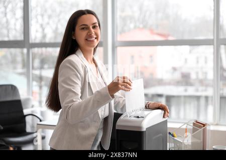 Junge Sekretärin, die Papierbogen mit dem Aktenvernichter im Büro zerstört Stockfoto