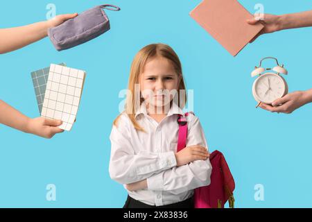 Verärgertes kleines Schulmädchen mit Rucksack und Händen, die den Wecker mit Notizbüchern auf blauem Hintergrund halten Stockfoto