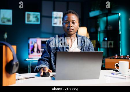 Junge afroamerikanische Freiberuflerin, die zu Hause auf ihrem digitalen Laptop arbeitet und Dokumente überprüft. Schwarze Frau, die am Schreibtisch sitzt, PC benutzt, E-Mails liest und beantwortet. Stockfoto