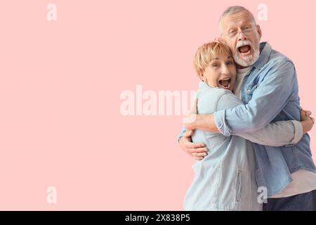 Reifes Paar umarmt sich mit fallendem Geld auf rosa Hintergrund Stockfoto