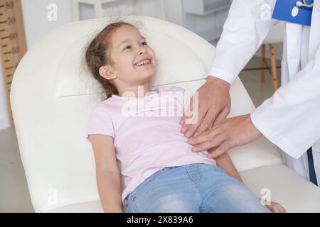 Männlicher Kinderarzt untersucht den Bauch des kleinen Mädchens auf der Couch in der Klinik, Nahaufnahme Stockfoto