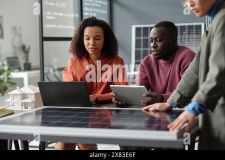 Zwei junge afroamerikanische Mitarbeiter mit Laptop und Tablet bereiten ein neues Geschäftsprojekt vor, während sie am Arbeitsplatz sitzen Stockfoto