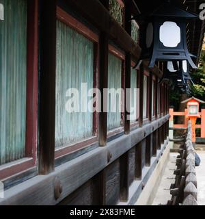 Nahaufnahme eines traditionellen japanischen Gebäudes mit Holzwänden und Metalllaternen. Das Gebäude verfügt über grün getönte Fenster und einen Holzzaun im Stockfoto