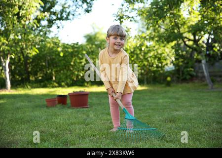 Süßes kleines Mädchen mit Rechen im Garten am Frühlingstag Stockfoto