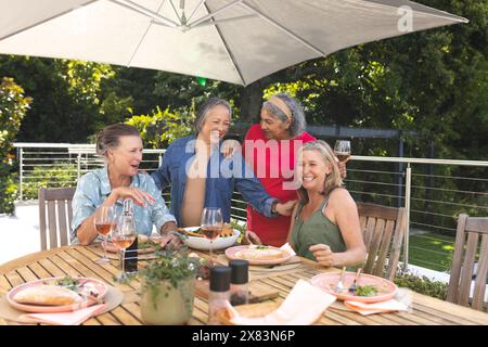 Verschiedene ältere Freundinnen genießen ein Mittagessen im Freien unter einem Sonnenschirm Stockfoto