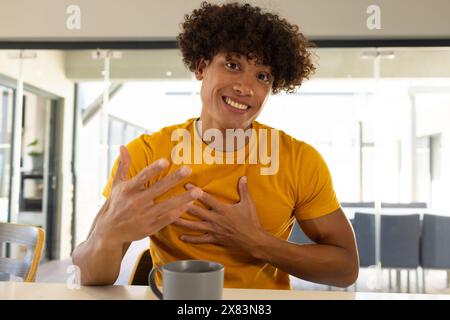 Ein birassischer junger Mann im Videogespräch zu Hause, der einen grauen Becher hält Stockfoto