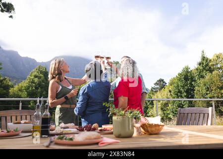 Verschiedene ältere Freundinnen, die am Tisch im Freien tosten Stockfoto