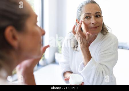 Im Badezimmer zu Hause, reife kaukasische Frau, die Creme auf das Gesicht aufträgt Stockfoto