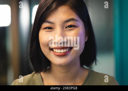 In einem modernen Büro für Geschäftsleute lächelt eine junge asiatische Frau im Innenbereich mit grünem Hintergrund Stockfoto